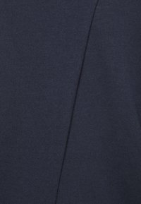 Tissu tricoté bleu marine avec une texture lisse, présentant un détail de couture diagonale. Le tissu semble doux et légèrement élastique.