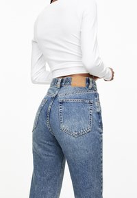 High-waisted blue jeans made of denim, featuring a light wash, five pockets, and a brown leather patch at the back waist.