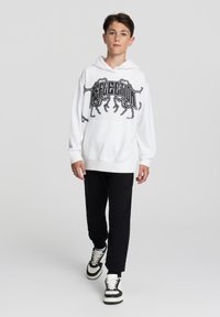 Felpa bianca con stampa grafica nera, pantaloni neri e sneakers bianco e nere. La felpa ha una tasca a marsupio frontale e polsini a costine.