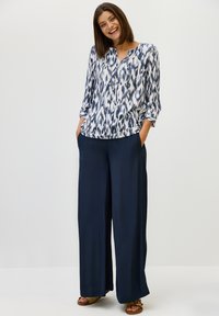 Blusa blanca fluida con patrón abstracto en azul marino, escote en V y mangas de tres cuartos, combinada con pantalones anchos en azul marino hechos de una tela suave.