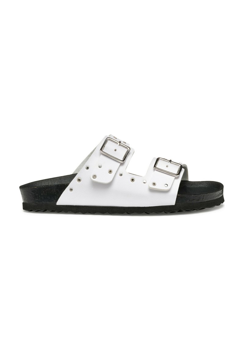 Sandalias blancas de dos correas con hebillas plateadas, suela texturizada negra y tachuelas decorativas a lo largo de las correas. Diseño plano con punta abierta.