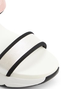 Hvid sandal med en tekstureret sølvrem med sort kant og en pink detalje. Sålen er let med en gummibelagt ydersål.