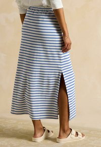 Paski maxi spódnica w białym i niebieskim bawełnianym materiale z elastycznym paskiem w talii i bocznym rozcięciem. Dobranie z lekkimi sandałami. Prosty, casualowy design.