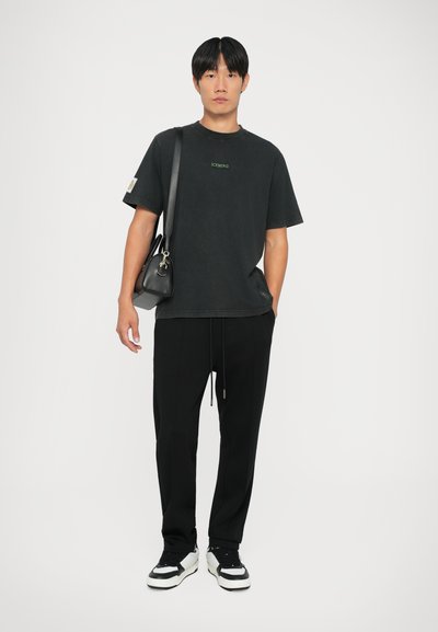 Sort oversized T-shirt med grønt "ICEBERG" logo, parret med sorte joggers, sorte sneakers med hvide accenter og en lille sort taske.
