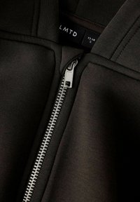 Crna zip-up jakna s srebrnim metalnim zatvaračem. Glatka tkanina s vidljivim detaljima šavova, oznaka pokazuje veličinu small (13-14).