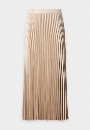 Jeune femme en haut noir sans manches et jupe plissée beige tenant une pochette crème, portant des ballerines noires à bout pointu avec une boucle.
