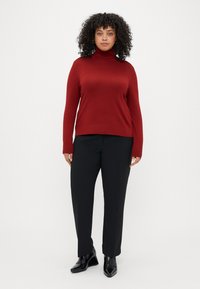 Bordo turtlenecks džemperis ar brīvu piegriezumu, valkāts kopā ar melniem taisnajiem biksēm un melniem norādītiem potīšu zābakiem. Gluda tekstūra, garas piedurknes.