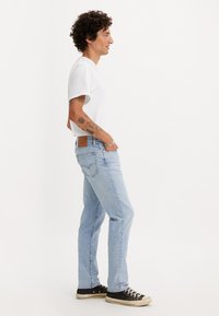 Lys blå jeans med rette ben, kombinert med en tettsittende hvit t-skjorte og svarte sneakers. Merkbar baklomme-design og brun lapp.