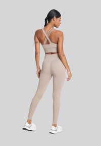 Beżowy zestaw odzieży sportowej z krótkim topem na ramiączkach w kształcie krzyża oraz legginsami z wysokim stanem; gładka textura i dopasowany fason.