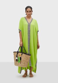 Limgrön kaftan med svart mönstrad kant. Vävda halmaccessoarer med färgglad tukanbroderi och svarta handtag. Platta sandaler.