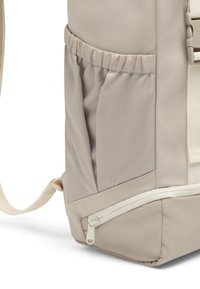 Bézs hátizsák, texturált nejlon anyagból, oldalsó hálós zsebbel és alsó részén fehér cipzárral záródó rekesszel.