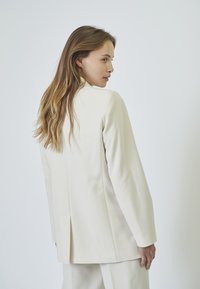 Ivory tailored blazer with a structured fit, long sleeves, notch collar, and back vent detail, made from smooth fabric.