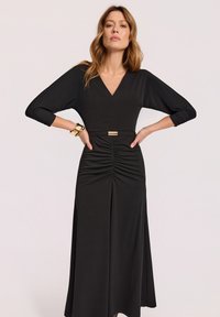 Czarna sukienka z głębokim dekoltem w serek, rękawami trójczworćowymi i marszczonymi detalami po boku. Gładki materiał z podkreśloną talią i złotymi akcentami.