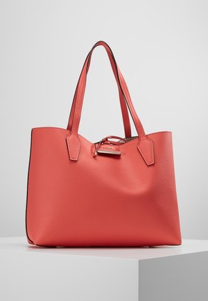 Korallenfarben strukturierte Leder-Shopper-Tasche mit zwei langen Griffen und einem kleinen Metallanhänger mit der Gravur "Guess" auf der Vorderseite.