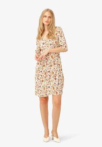 Floral wrap dress in light fabric with a V-neck, three-quarter sleeves, and a belted waist, featuring a multicolored pattern on a cream background.