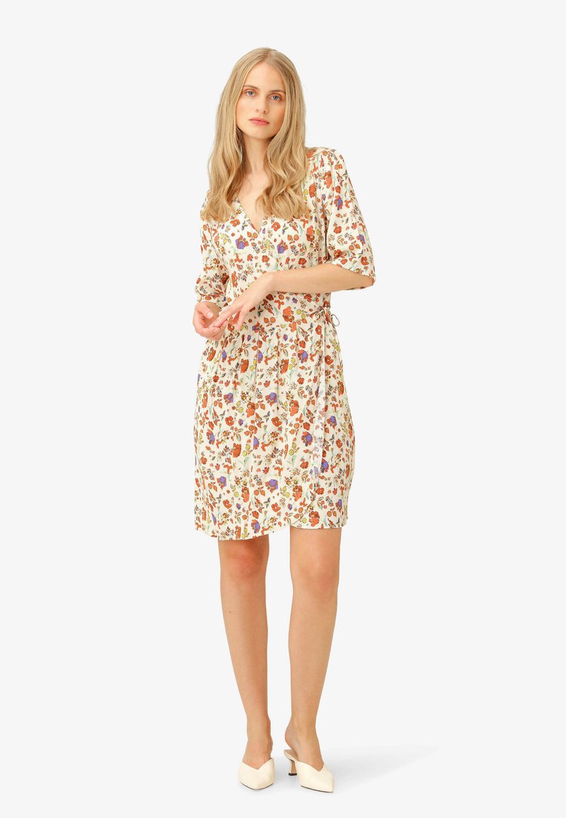 Floral wrap dress in light fabric with a V-neck, three-quarter sleeves, and a belted waist, featuring a multicolored pattern on a cream background.