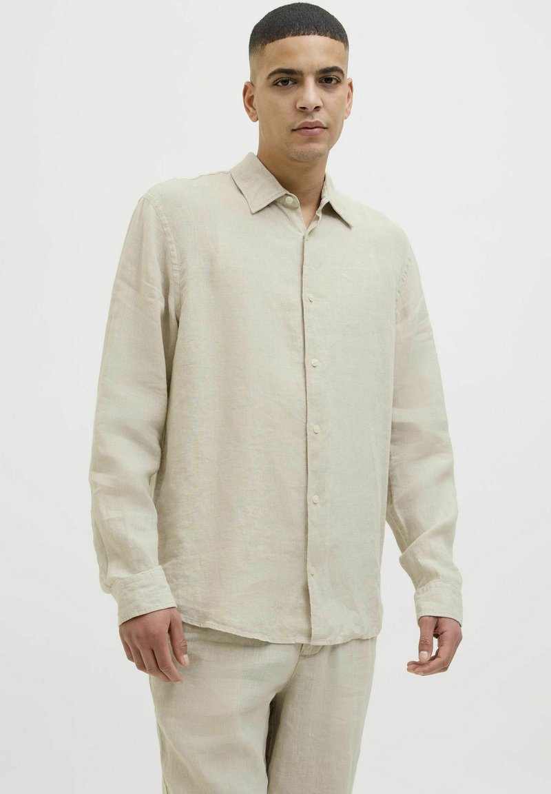 Camisa de lino beige de botones con cuello clásico, mangas largas y una textura sutil. Presenta undo recto y cierre de botón en la parte frontal.