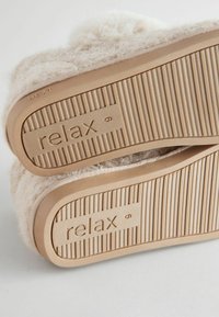 Beige obuv s huňatým svrškem, texturovanou gumovou podrážkou a slovem "relax" vylisovaným na boku. Na podrážce jemný drážkovaný vzor.