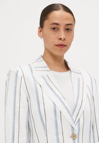 Striped blazer in white with light blue and brown lines, featuring a single button and a notched lapel. Made of lightweight linen fabric.