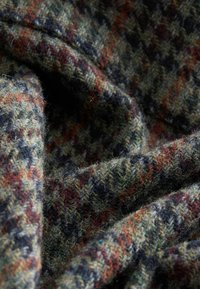 Multifarvet hounds-tooth uldstof med en blød, tekstureret overflade. Farverne inkluderer grøn, brun og sporadiske nuancer af rød og blå.
