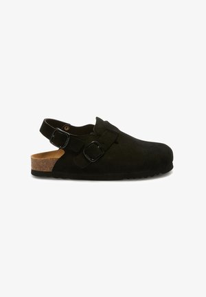 Zoccoli in suede nero con due fibbie regolabili e una parte posteriore aperta, su un piede in sughero e suola in gomma.