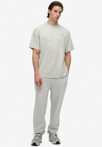 Hellgraues Baumwoll-T-Shirt und passende Jogginghose. Einfaches Design mit lockerer Passform. Akzentuiert durch ein kleines Logo auf der Brust. Sneaker inklusive.