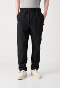 Svarte bukser med elastisk midje, sidelommer, innsvingt design og lett materiale. Kombinert med hvite joggesko.