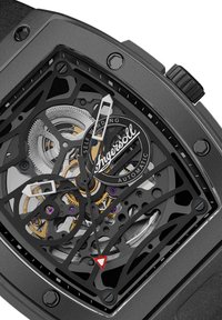 Vierkante zwarte horloge met een openwerk dial met zilveren tandwielen, paarse accenten en witte wijzers. Zelfopwindmechanisme zichtbaar.