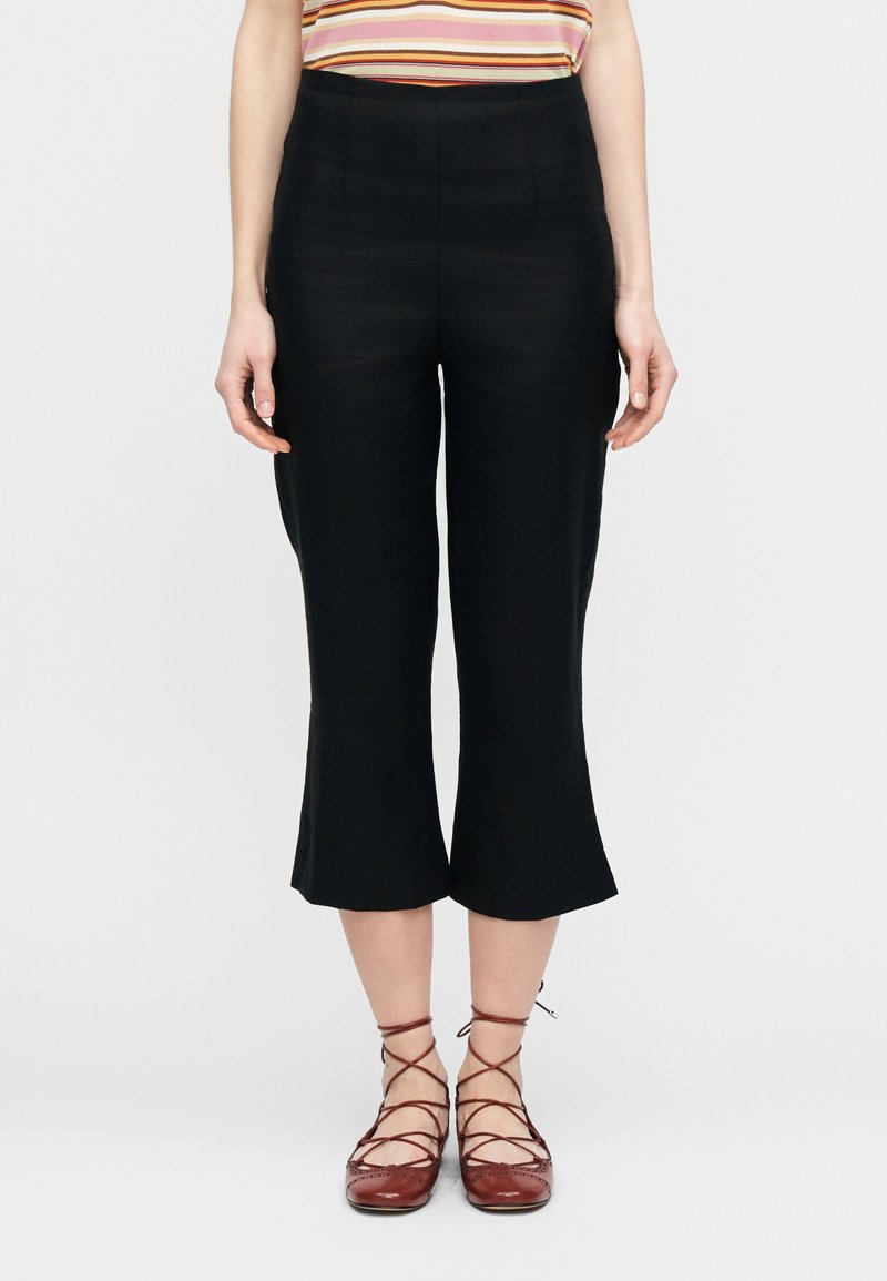 Μαύροι κοντοί παντελόνες με φαρδιά ρεβέρ, με λεία υφή και ψηλή μέση. Συνδυασμένοι με κόκκινα παπούτσια με κορδόνια.