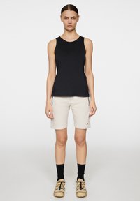 Svart ärmlös linne kombinerat med beige shorts. Outfiten har en subtil logotyp på shortsen och ett texturerat, lätt tyg.