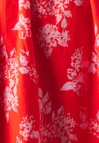 Punane kangas valge lillemustriga. Sile tekstuur, kergelt läbipaistev välimus, suured lilled ja lehed.