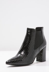 Botín negro de tobillo fabricado en un material texturizado con un patrón de piel de serpiente, punta afilada, paneles laterales elásticos y un tacón grueso.