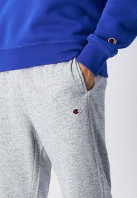 Blå sweatshirt med ribbad krage, kombinerad med grå mjukisbyxor med en logotyp-patch. Tyget verkar mjukt och bekvämt.