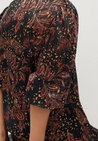 Blusa ligera negra con un patrón de paisley floral en rojo, verde y beige, que presenta un diseño plisado y mangas cortas con puños.