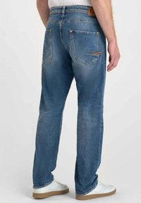 Jean en denim bleu avec une coupe droite, deux poches arrière et une finition texturée. Présente une étiquette en cuir marron au niveau de la taille.