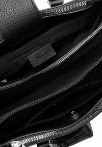 Svart läderhandväska inuti med flera dragkedjefack och en texturerad yta, med ett tygfoder.