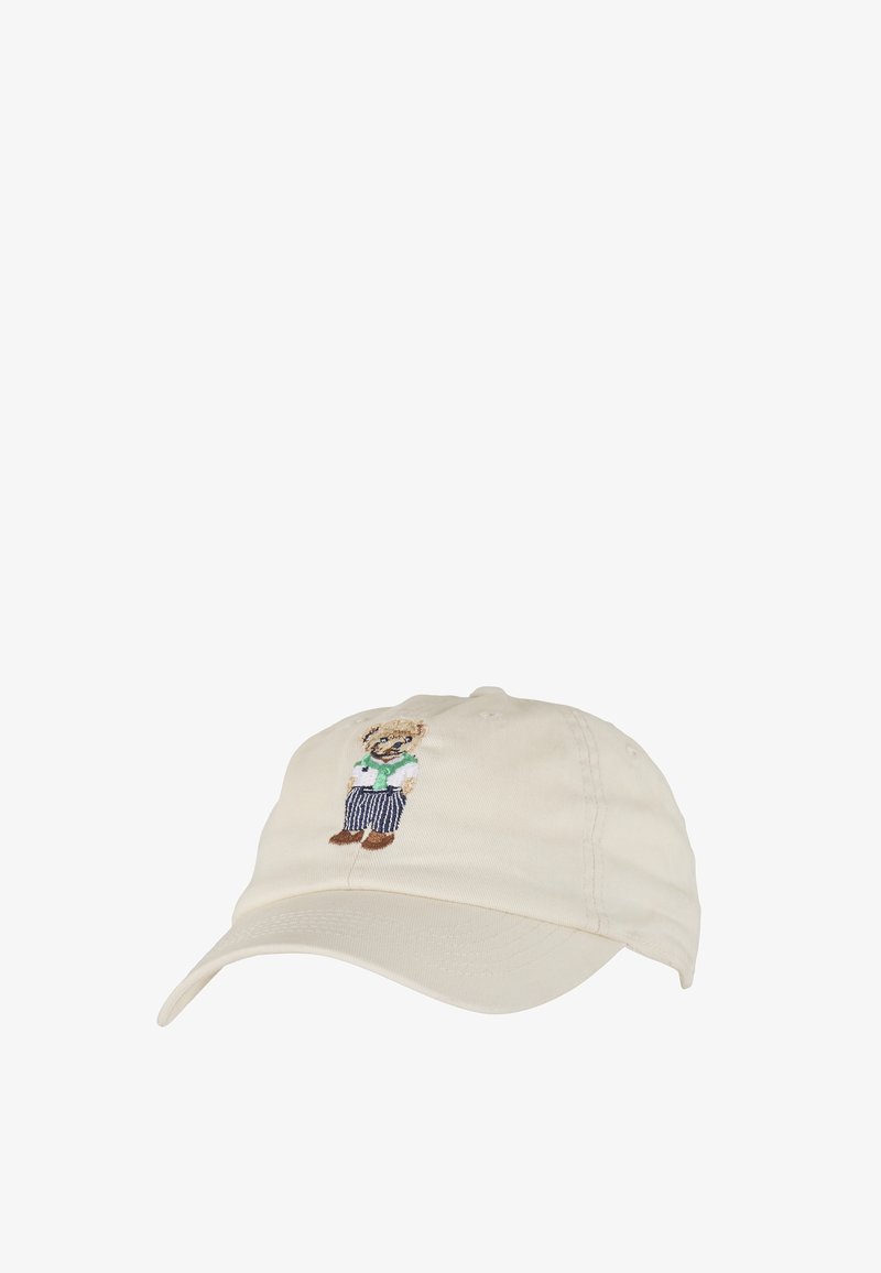 Casquette de baseball beige avec un ours brodé portant des lunettes de soleil, un gilet vert, une chemise blanche, un pantalon rayé et des chaussures marron au centre devant.
