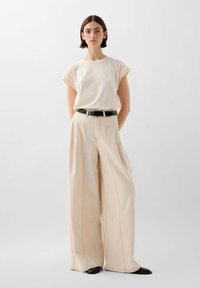 T-shirt beige a maniche corte abbinato a pantaloni beige larghi. I pantaloni presentano una vita alta e passanti per la cintura, completati da una cintura nera.
