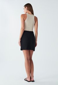 Béžový rebrovaný top bez rukávov v kombinácii s čiernou mini sukňou, ktorá predvádza priliehavý strih a hladkú textúru, so zapínaním na zips na boku.