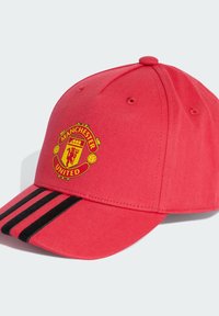 Červená baseballová čiapka s ohnutým okrajom, na prednej strane s logom Manchester United a dvoma čiernymi pruhmi pozdĺž okraja.