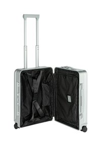 Maleta rígida plateada con apertura de doble cremallera; el interior presenta un tejido negro con patrón hexagonal, correas ajustables y múltiples bolsillos.