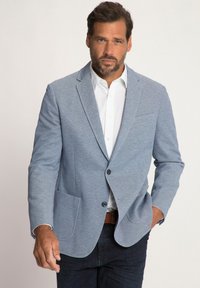 Blazer azzurro chiaro con tessuto a trama, chiusura a un bottone, due tasche frontali, indossato sopra una camicia bianca e jeans scuri.