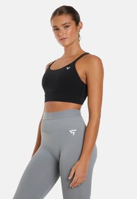 Zwarte sportbeha met dunne bandjes, met een logo aan de voorkant. Gecombineerd met hoog-wijde grijze leggings, met een gladde textuur en een aansluitend ontwerp.