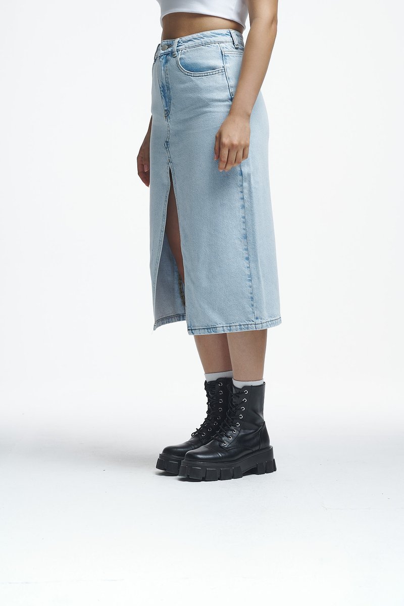 Ανοιχτό μπλε τζιν μίντι φούστα με μπροστινή σχισμή, ψηλή μέση και κλείσιμο με κουμπί, συνδυασμένη με μαύρες χοντρές μπότες με κορδόνια. Λείο υλικό.
