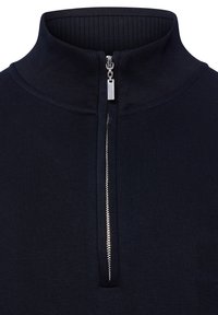 Hochkragenpullover in Marineblau mit silbernem Reißverschluss, der an der vorderen Mitte des Kragens teilweise geöffnet ist.