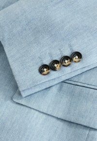 Light blue blazer sleeve with four dark brown gradient buttons sewn on near the cuff.