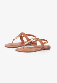 Sandali piatti in pelle marrone con design a fascia per le dita, caratterizzati da accentuazioni circolari dorate lungo le cinghie e un tacco basso in legno.