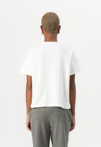 White short-sleeve top with a relaxed fit, made of smooth fabric. The design features a round neckline and a straight hemline.