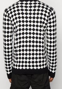 Pletený svetr s černo-bílým diamantovým vzorem, s kulatým výstřihem, žebrovanými manžetami a lemem. Vyrobený z měkké, texturované látky.