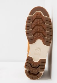 Semelle d'une botte beige avec des crampons profonds, arborant un logo Timberland et la marque SENSORFLEX au centre.
